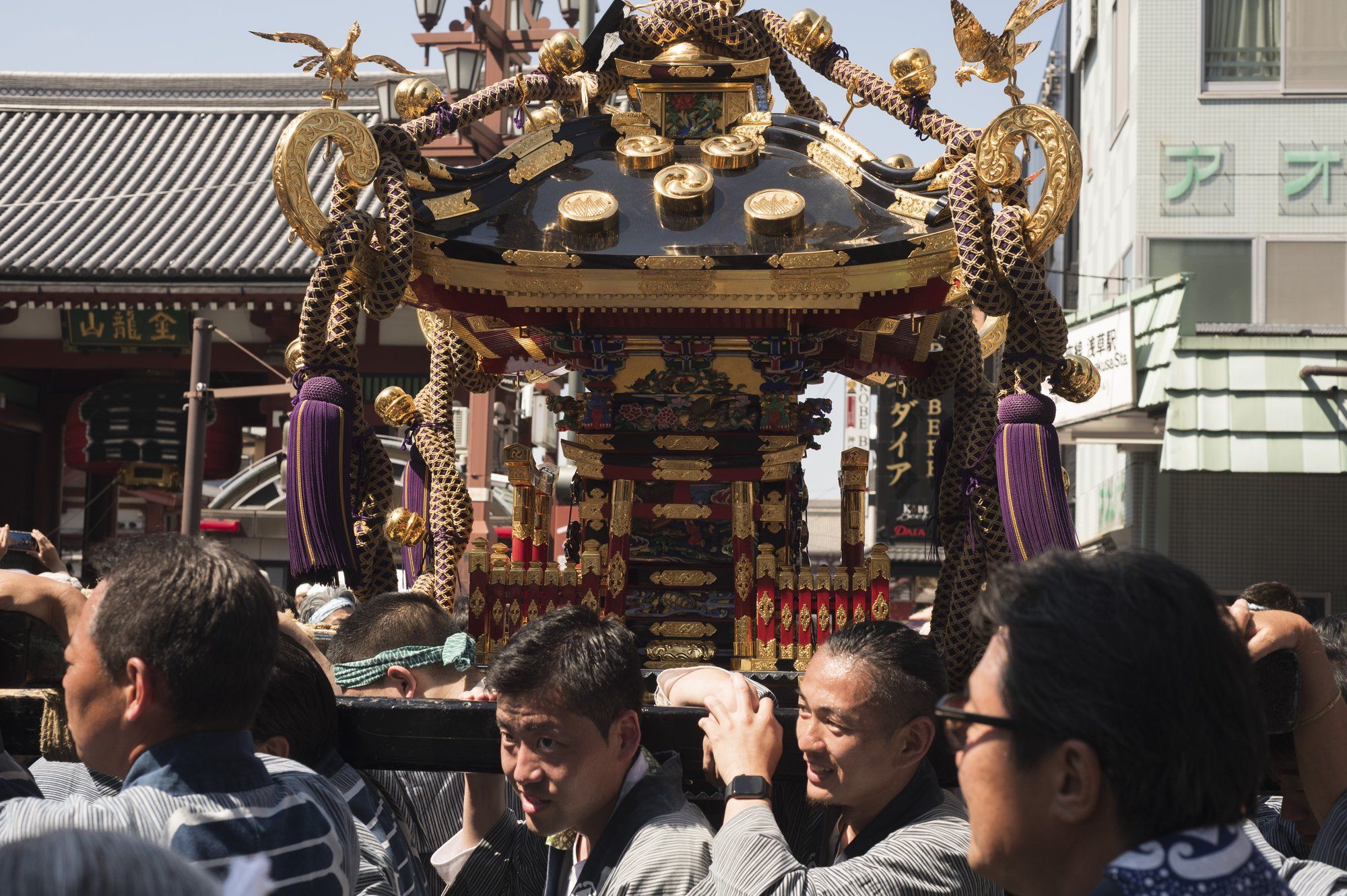 Men in matching happi coats carrying a golden mikoshi in Asakusa.