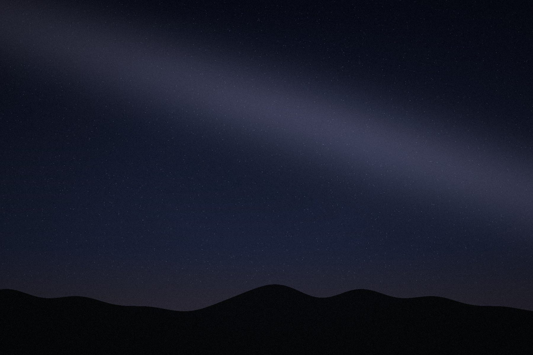 Stars and a faint band of light above a dark hill.